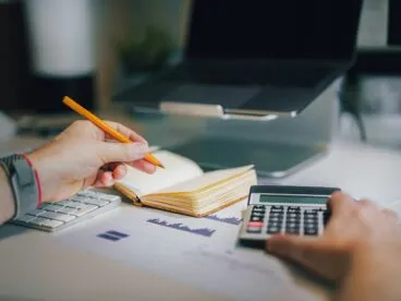 A person sitting at a desk with a pen and a calculator