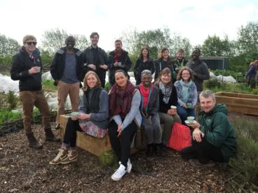 Students from a programme sitting outside. They are sitting on raised beds in a garden.