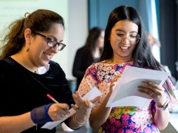 Two people with paper and pencils in their hands smiling and working together