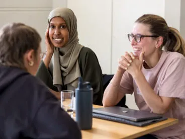 Three people at a table smiling and having a discussion.